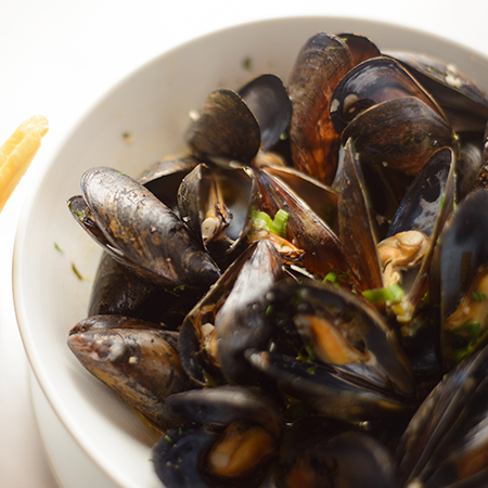 A bowl filled with mussels and side of fries in a cup.